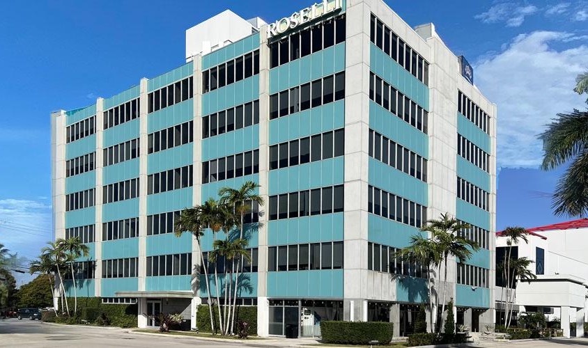 The Roselli Building: a six-storey office building on North Federal Highway with bands of teal glass, a pale concrete frame, and ROSELLI lettering across the roofline.